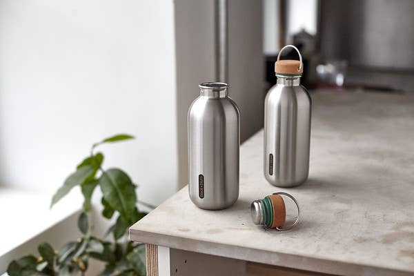 Two stainless steel water bottles with wooden caps on a table indoors.