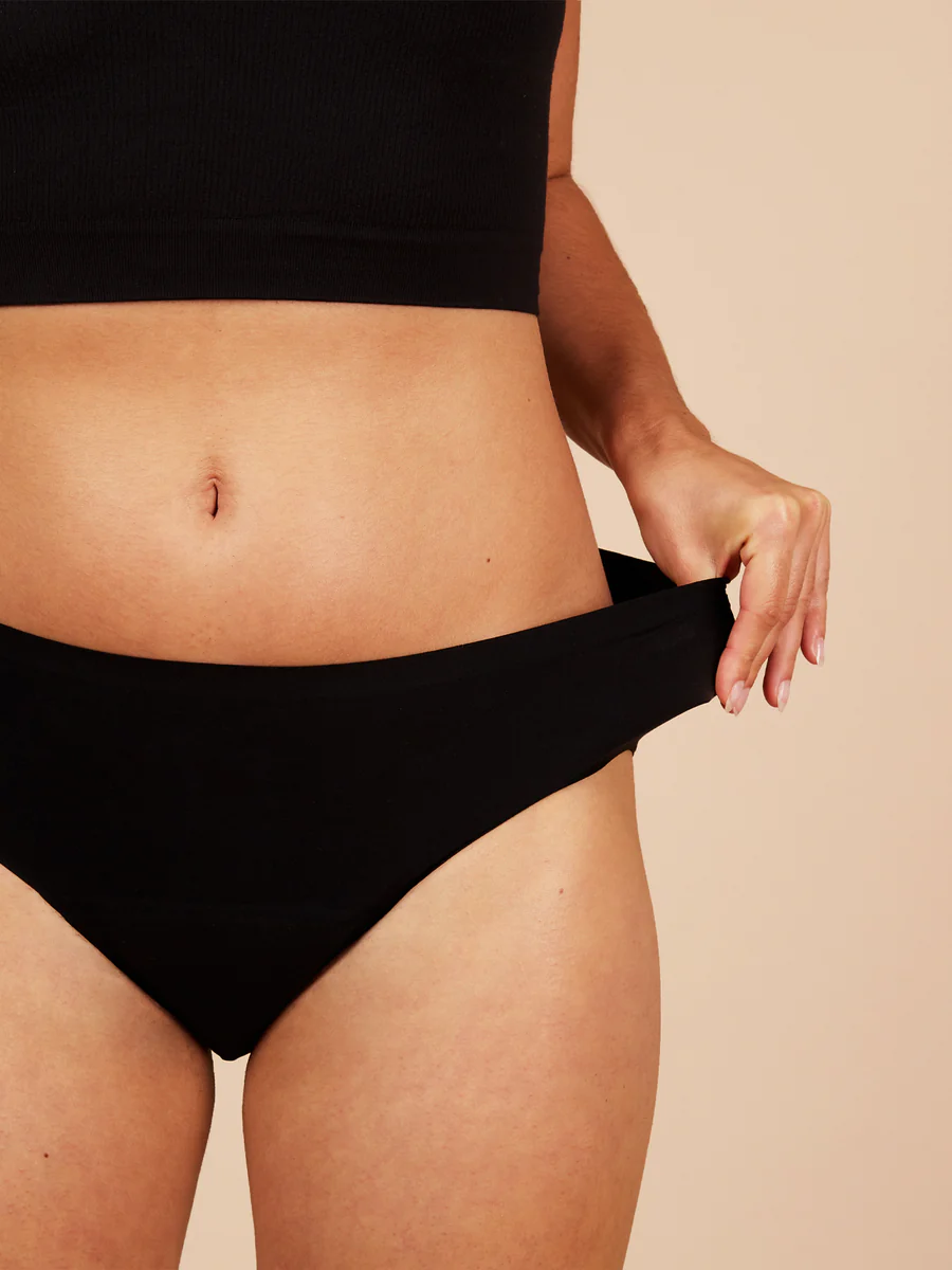 Person wearing black high-waisted briefs on a beige background