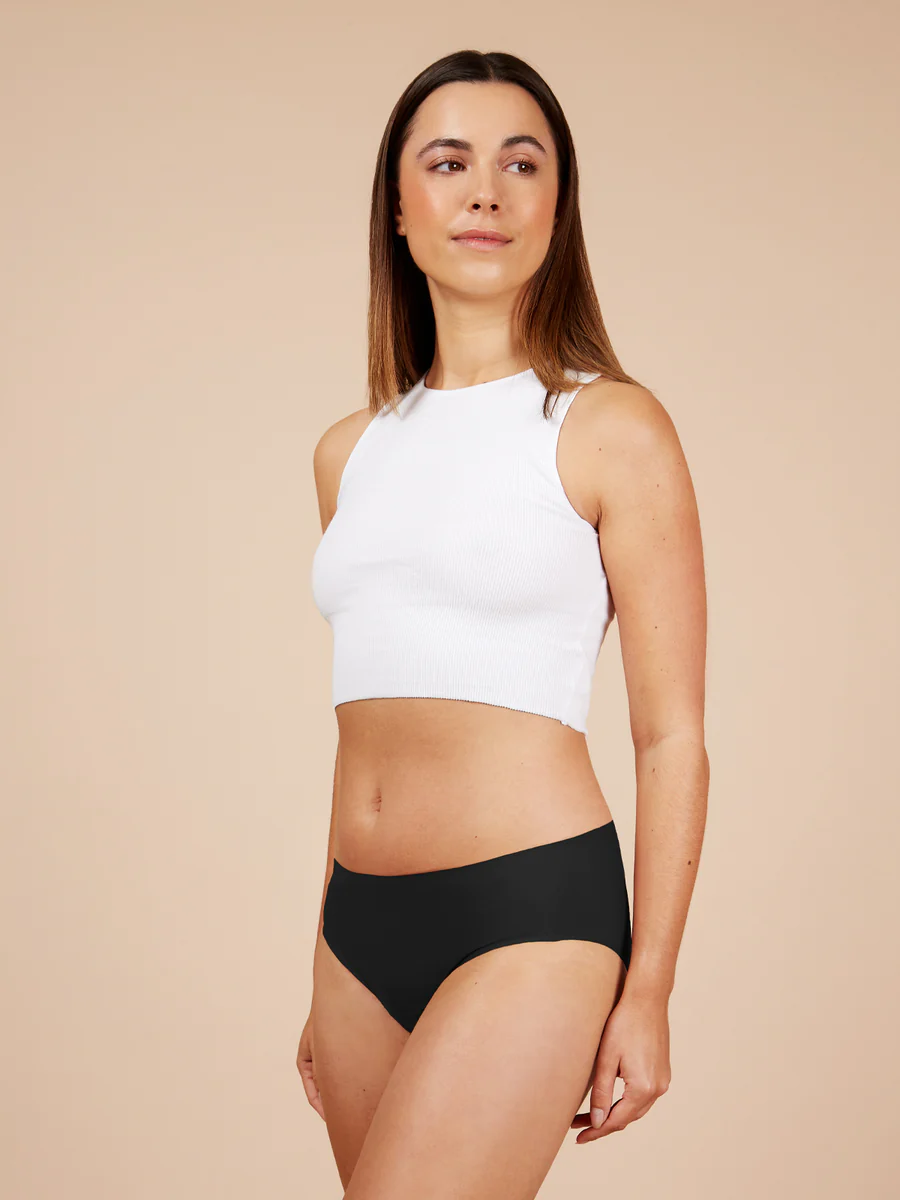 Woman wearing a white sleeveless top and black high-waisted underwear on a beige background