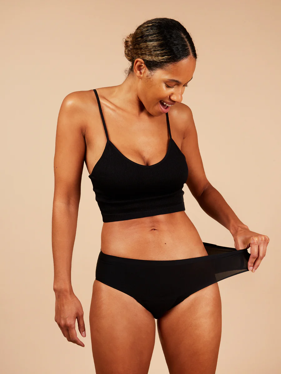 Woman wearing a black stretchy briefs on a beige background