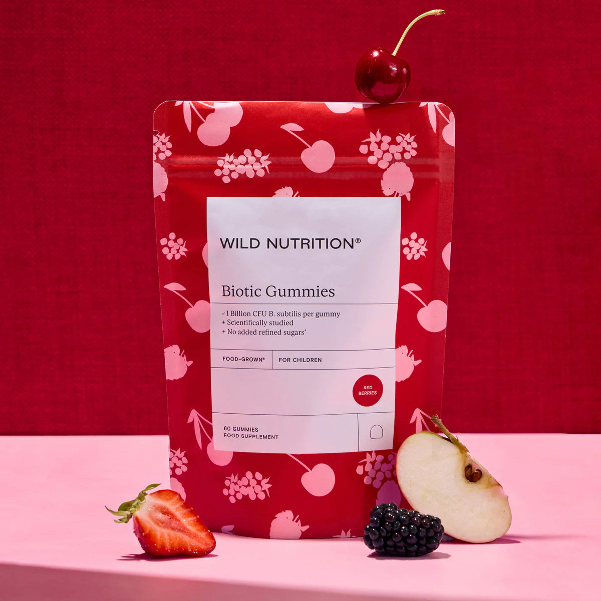 Red package of Wild Nutrition Biotic Gummies with a cherry on top against a red background