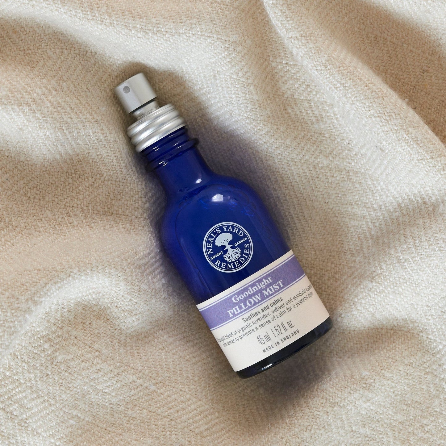 Blue bottle of Goodnight Pillow Mist on beige fabric